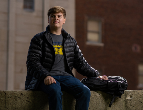 student sitting on a short wall at dusk